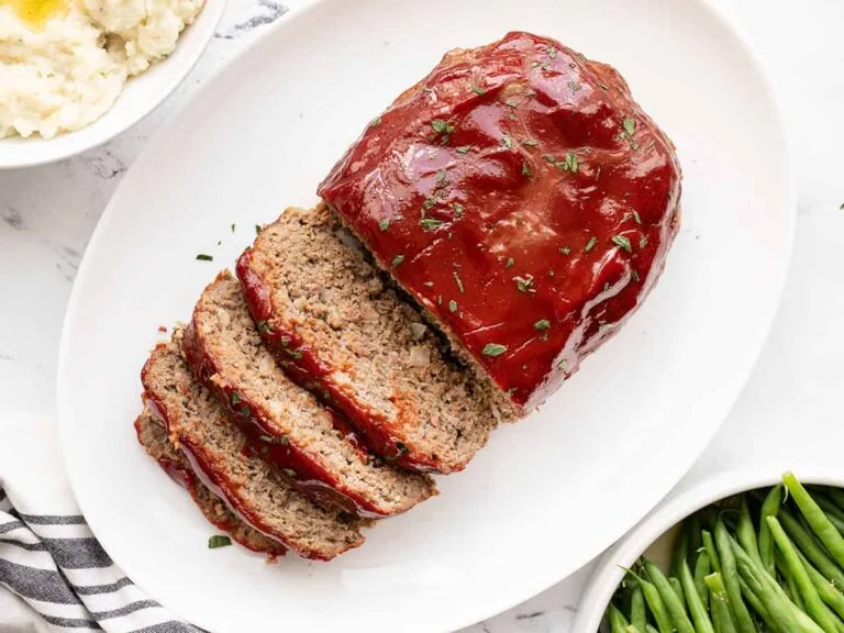 "Classic Homemade Meatloaf: A sliced meatloaf topped with ketchup glaze, served on a plate with vegetables"